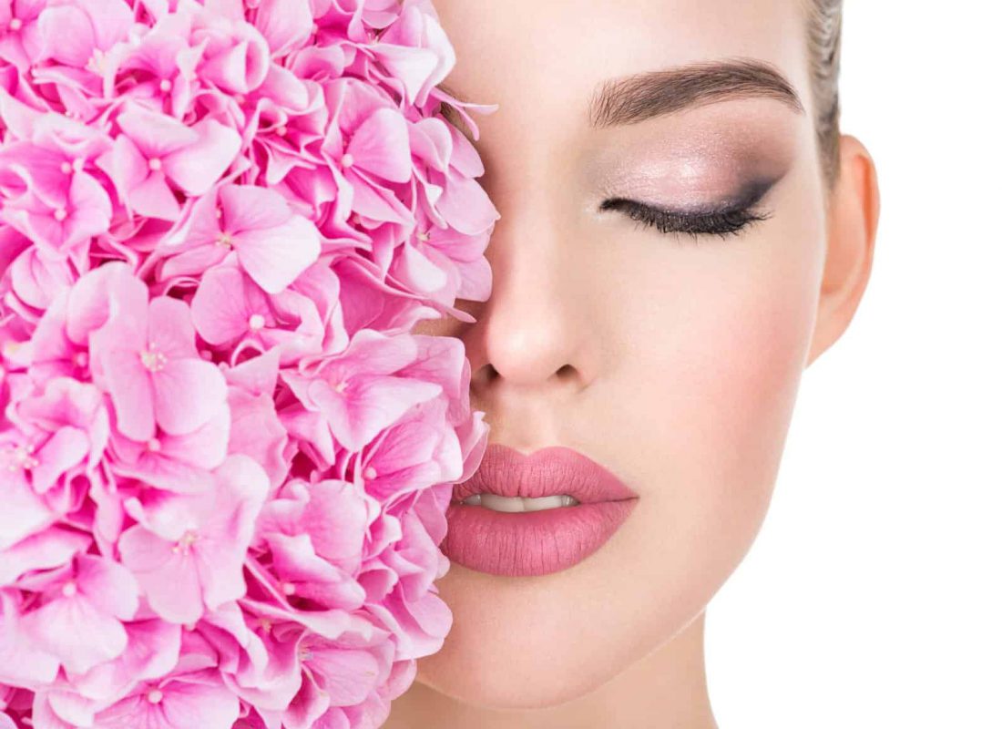 Young beautiful woman with flowers near face. Beauty treatment concept. Skin care. Pretty female with health, fresh skin of body. Lady with pink makeup of eyes.